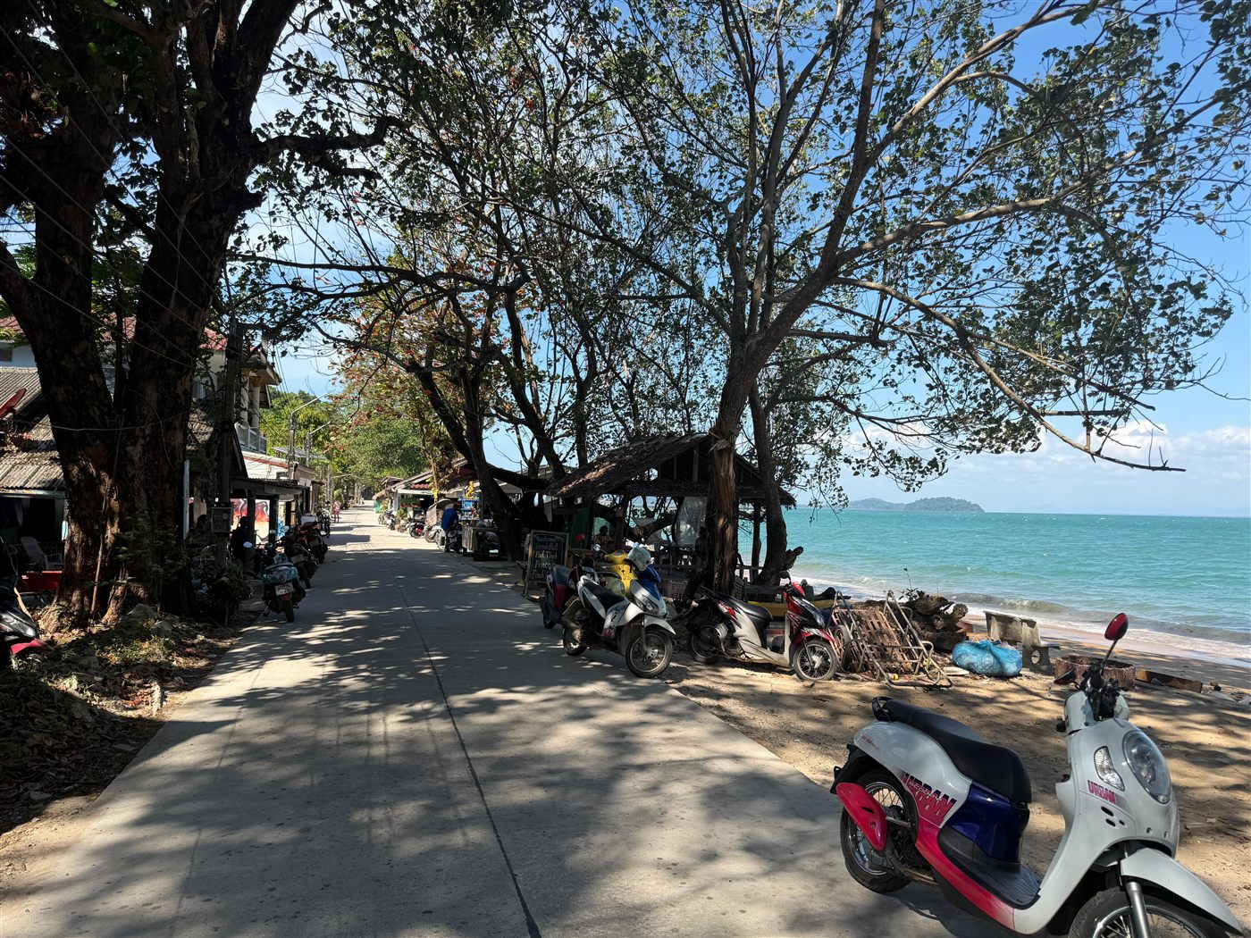 Strandpromenade auf Koh Phayam mit geparkten Mopeds und Meerblick